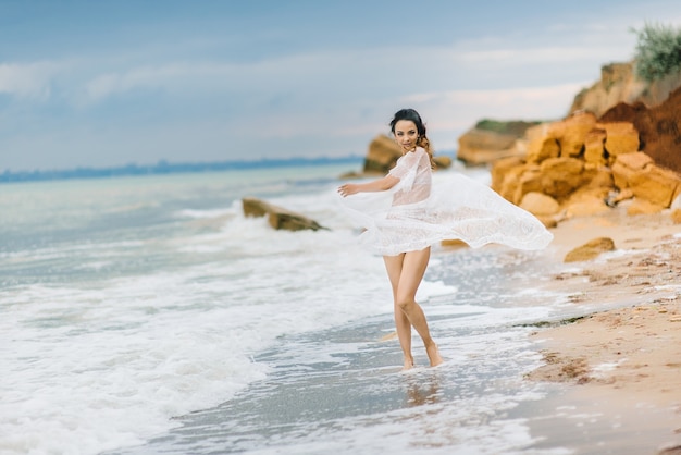 Novia en ropa interior y una bata con velo camina por la playa