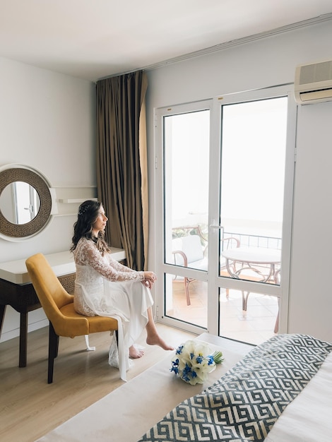 Foto la novia se sienta en una silla en una habitación de hotel y mira a la calle a través de la puerta del balcón