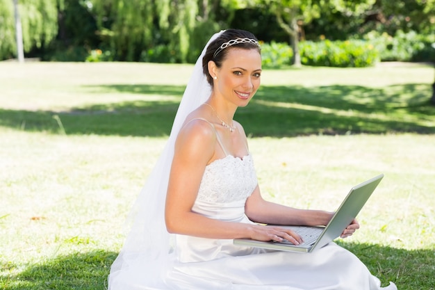 Novia sonriente que usa la computadora portátil en jardín