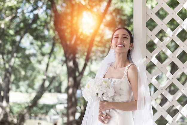 Foto novia sonriente sosteniendo un ramo de flores de pie contra los árboles en el parque