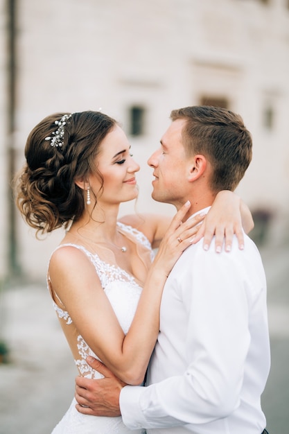 Novia sonriente con un vestido de encaje blanco abraza al novio por el cuello. El novio abraza la cintura de la novia. De cerca. Foto de alta calidad