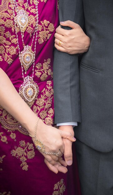 Novia sosteniendo la mano del novio cerca de la foto Joyas de oro y vestido morado de regreso a casa