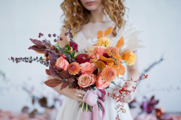 La novia sostiene un hermoso ramo de otoño con flores y bayas naranjas y rojas