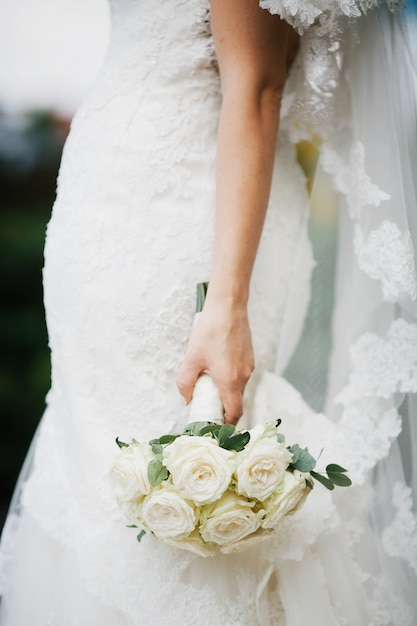 La novia sostiene la mano con ramo de boda abajo parado afuera
