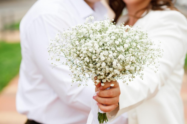 La novia sostiene el ramo blanco de su boda en la naturaleza.