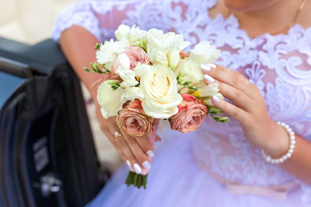 La novia sostiene un ramo de novia en la mano contra el fondo de un vestido blanco