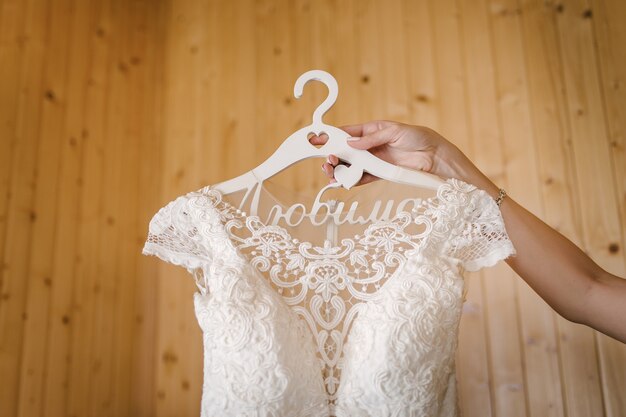 La novia sostiene el vestido de novia en la percha con la mano