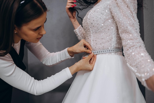 La novia en la tienda de ropa para vestidos de novia está eligiendo un vestido y el diseñador la está ayudando