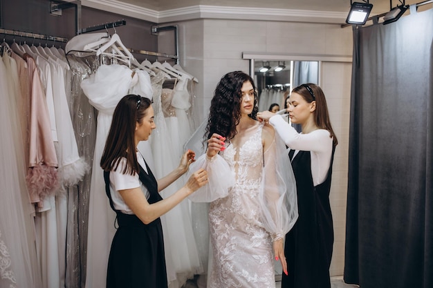 La novia en la tienda de ropa para vestidos de novia está eligiendo un vestido y el diseñador la está ayudando