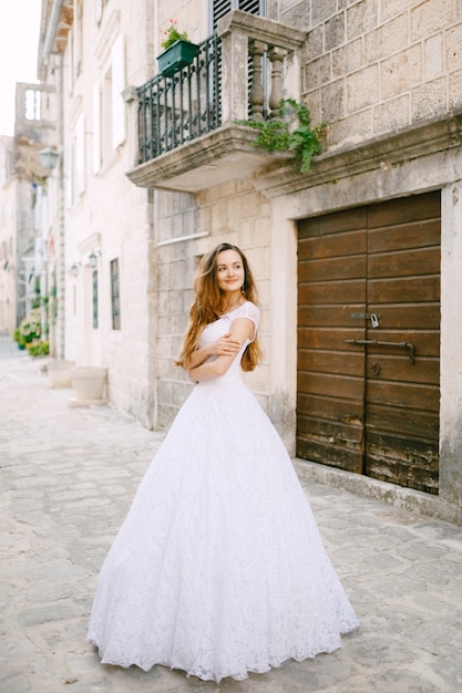 La novia con un tierno vestido de novia se encuentra cerca de un hermoso edificio antiguo en Perast. Foto de alta calidad