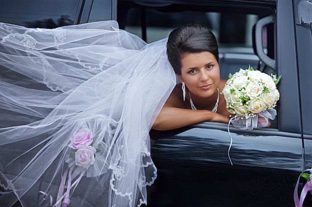 La novia con el velo ondeante mira desde la ventana de un auto