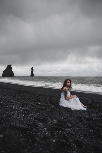 novia vestida de blanco se encuentra en una playa de arena negra cerca del Océano Atlántico en Islandia