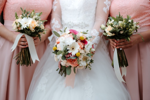 La novia vestida de blanco tiene un hermoso ramo de novia con novias vestidas de rosa