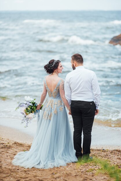 novia en un vestido azul caminar a lo largo de la orilla del mar