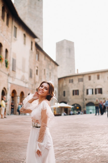 Una novia con un vestido blanco en el casco antiguo de San Gimignano. Una niña camina por la ciudad en Italia. Toscana.
