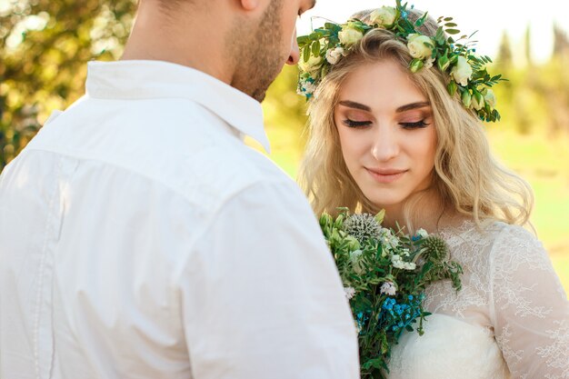 Novia en vestido blanco y corona y retrato del novio en un día soleado de verano Boda rústica al aire libre