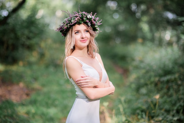 La novia en el vestido blanco ligero se coloca en guirnalda en el bosque