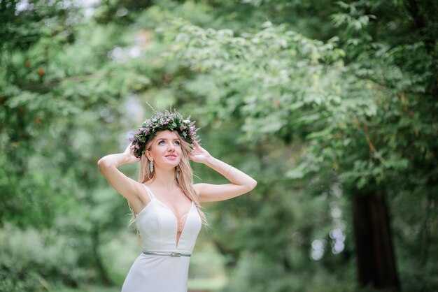 La novia en el vestido blanco ligero se coloca en guirnalda en el bosque