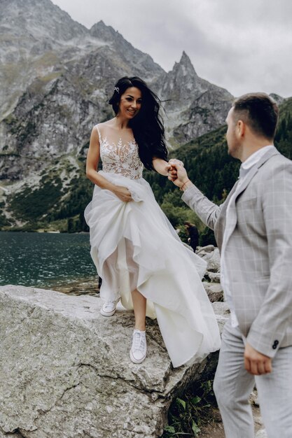 La novia con un vestido blanco y el novio de pie cerca del río y abrazando y sol