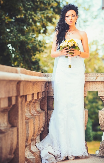 Novia con vestido blanco de pie en el balcón por la mañana Hermosa novia en la terraza Mañana de la novia