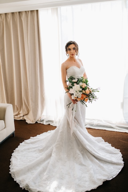 Novia con un vestido blanco con un ramo de flores en una habitación de hotel