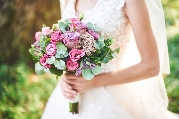 Novia con un vestido blanco con un ramo de flores púrpuras y vegetación