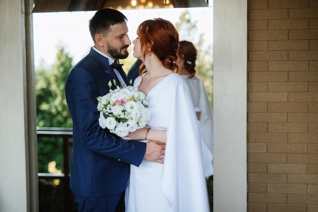 La novia con un vestido blanco con un ramo y el novio con un traje azul.