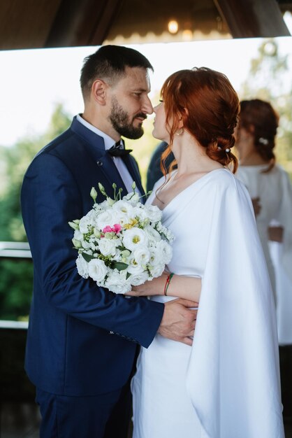 La novia con un vestido blanco con un ramo y el novio con un traje azul.