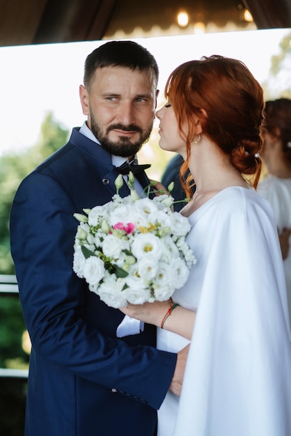 La novia con un vestido blanco con un ramo y el novio con un traje azul.