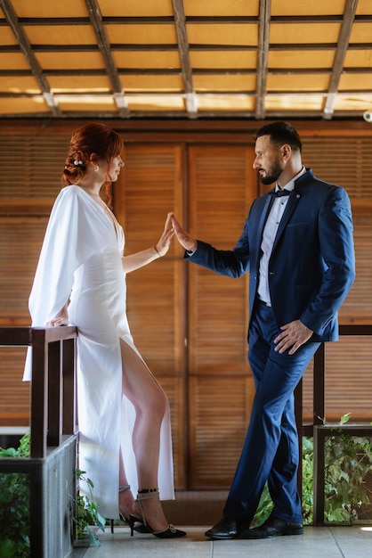 La novia con un vestido blanco con un ramo y el novio con un traje azul.