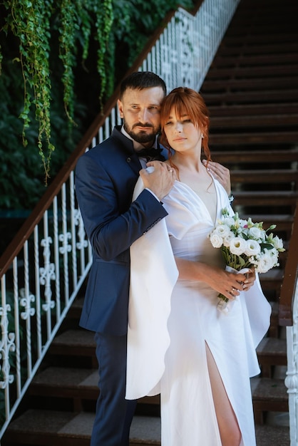 La novia con un vestido blanco con un ramo y el novio con un traje azul.