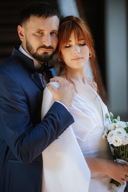 La novia con un vestido blanco con un ramo y el novio con un traje azul.