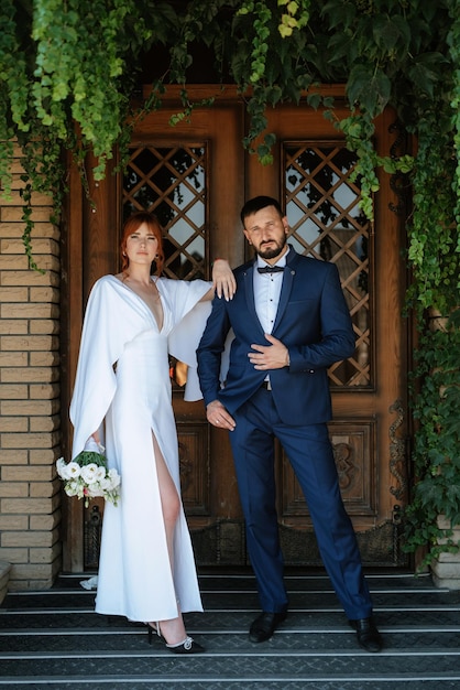 La novia con un vestido blanco con un ramo y el novio con un traje azul.