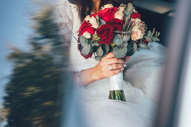 novia en vestido blanco con ramo de rosas rojas