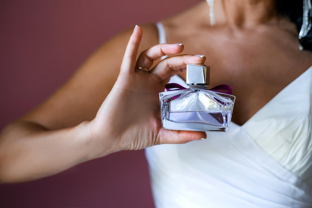 La novia con un vestido blanco sostiene una hermosa botella de perfume