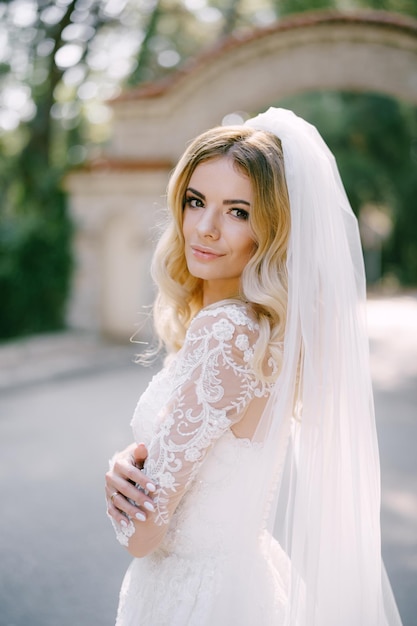 La novia con un vestido de encaje blanco con un velo se encuentra frente a un retrato de arco de piedra