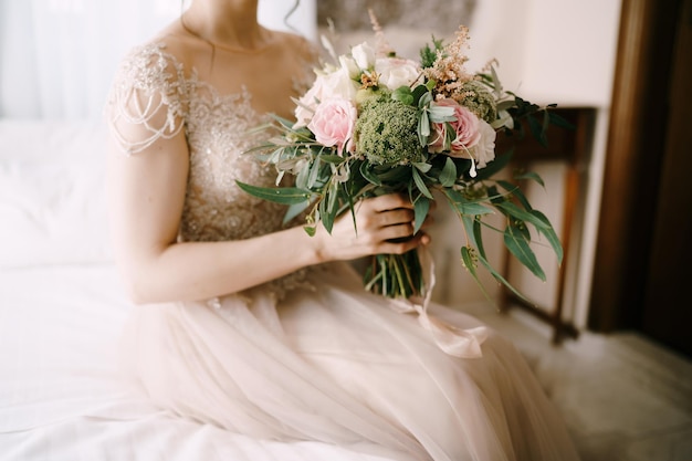 Novia con un vestido de encaje con un hermoso ramo de flores se sienta en la cama