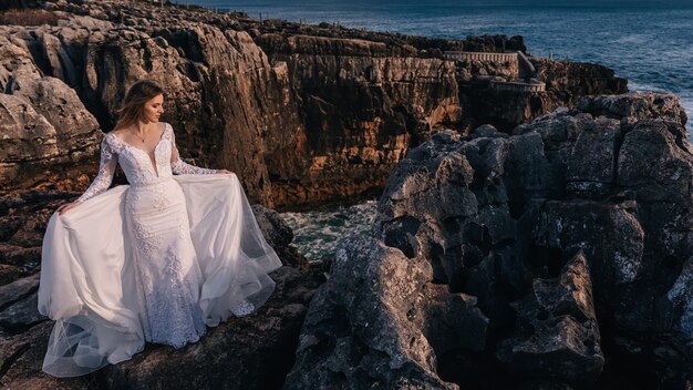 Novia en vestido de novia blanco cerró los ojos en el fondo de las rocas y el mar