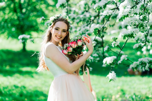 La novia en vestido de novia blanco sostiene un ramo en el parque verde. Boda de verano en un día soleado.