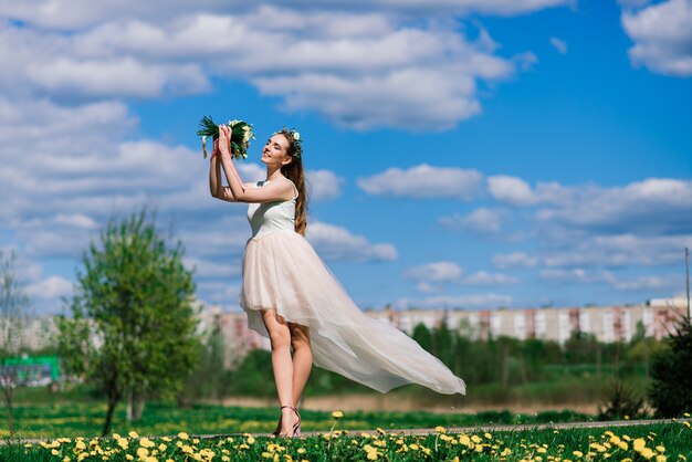 La novia en vestido de novia blanco sostiene un ramo en el parque verde. Boda de verano en un día soleado.