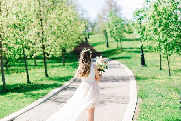 La novia en vestido de novia blanco sostiene un ramo en el parque verde. Boda de verano en un día soleado.