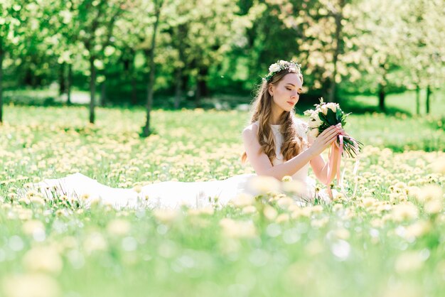 La novia en vestido de novia blanco sostiene un ramo en el parque verde