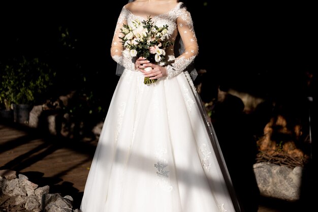 La novia con un vestido de novia blanco sostiene su ramo de novia en sus manos.