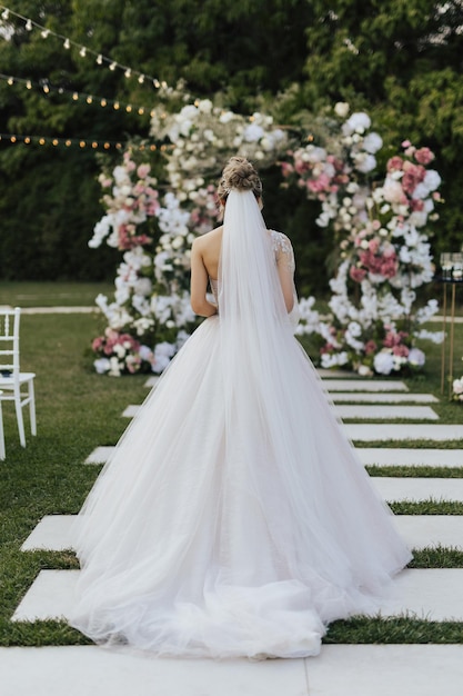 Una novia con un vestido de novia se para frente a un arco floral.