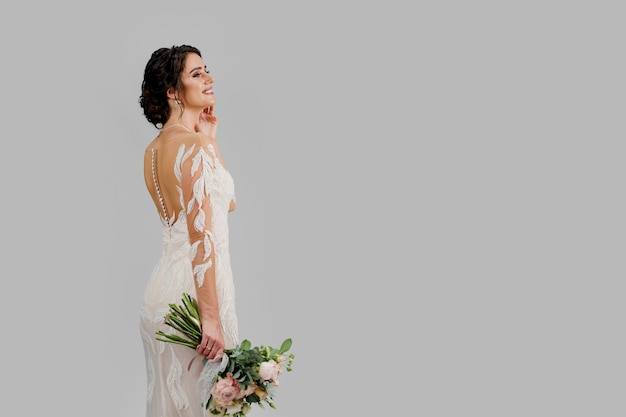 Novia en vestido de novia de lujo con ramo de flores en estudio en el lado derecho de la pared blanca en blanco. Anuncio para redes sociales para agencia de bodas y salón de novias.