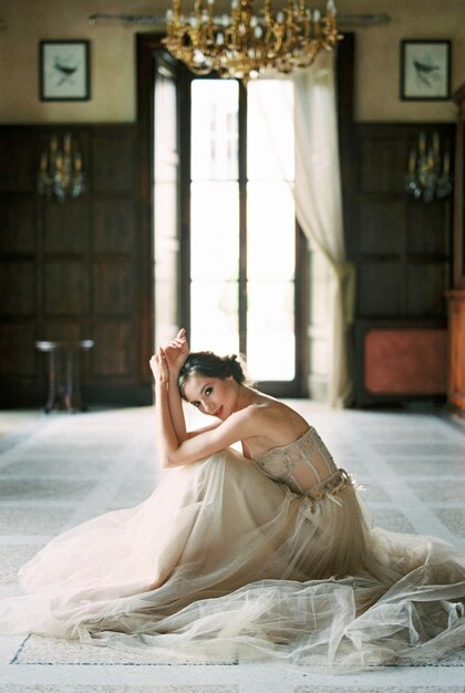 Foto la novia en un vestido se sienta en el suelo cerca de la ventana de una vieja villa