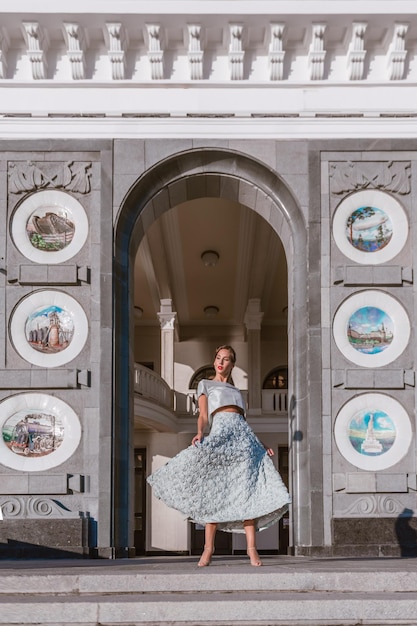 La novia con un vestido de tafetán turquesa suavemente baila en el porche del edificio con una arquitectura original