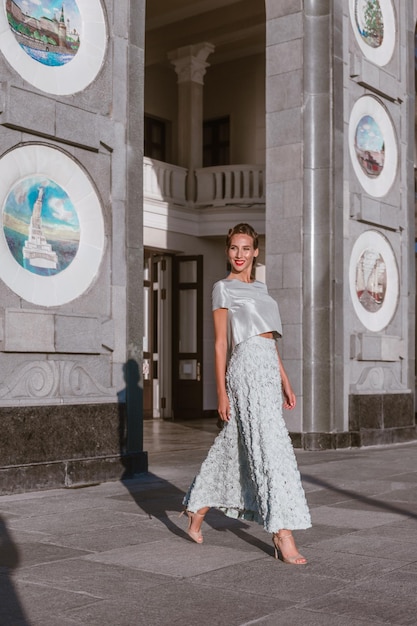 La novia con un vestido de tafetán turquesa suavemente baila en el porche del edificio con una arquitectura original