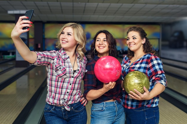 Foto novias felices toman selfie con teléfono inteligente en el club de bolos