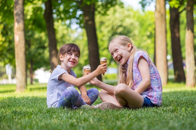 Novias de niñas sonrientes sentados en el césped y comiendo helado. vacaciones de los niños